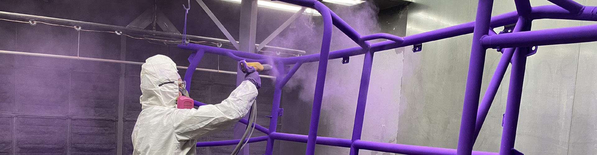 person applying purple powder coat to metal bars